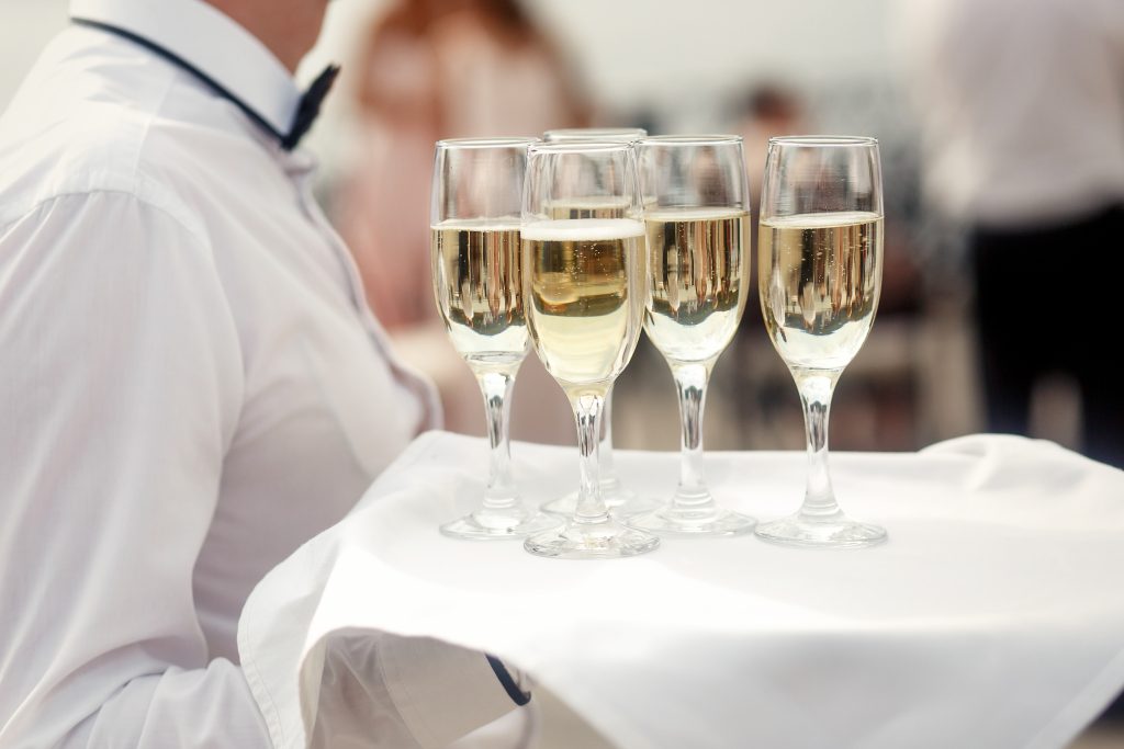Waiter in white carries tray with champagne flutes